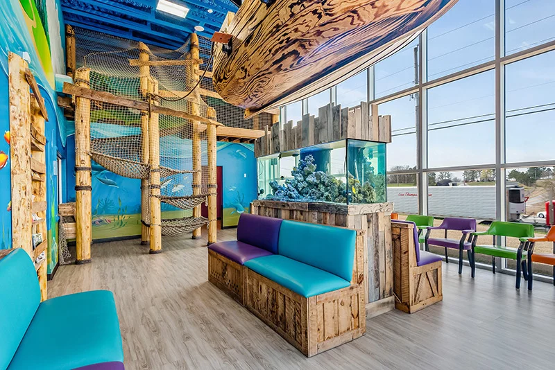 The Super Smiles waiting room — a 30-foot pirate ship hangs over a fish tank, with a rope-gym hideout above and aqua bench seating below