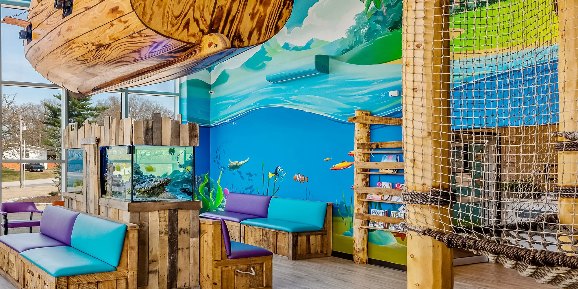 The Super Smiles lobby — rope-net climbing apparatus, fish tank, pirate-ship hideout, and aquatic banquette seating in one frame